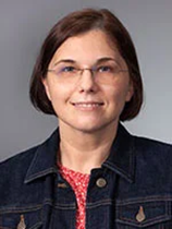 An image of Dr. Elizabeth Szatmari. She has chin-length brown hair, pale skin, and glasses. She is wearing a jean jacket. She is smiling.