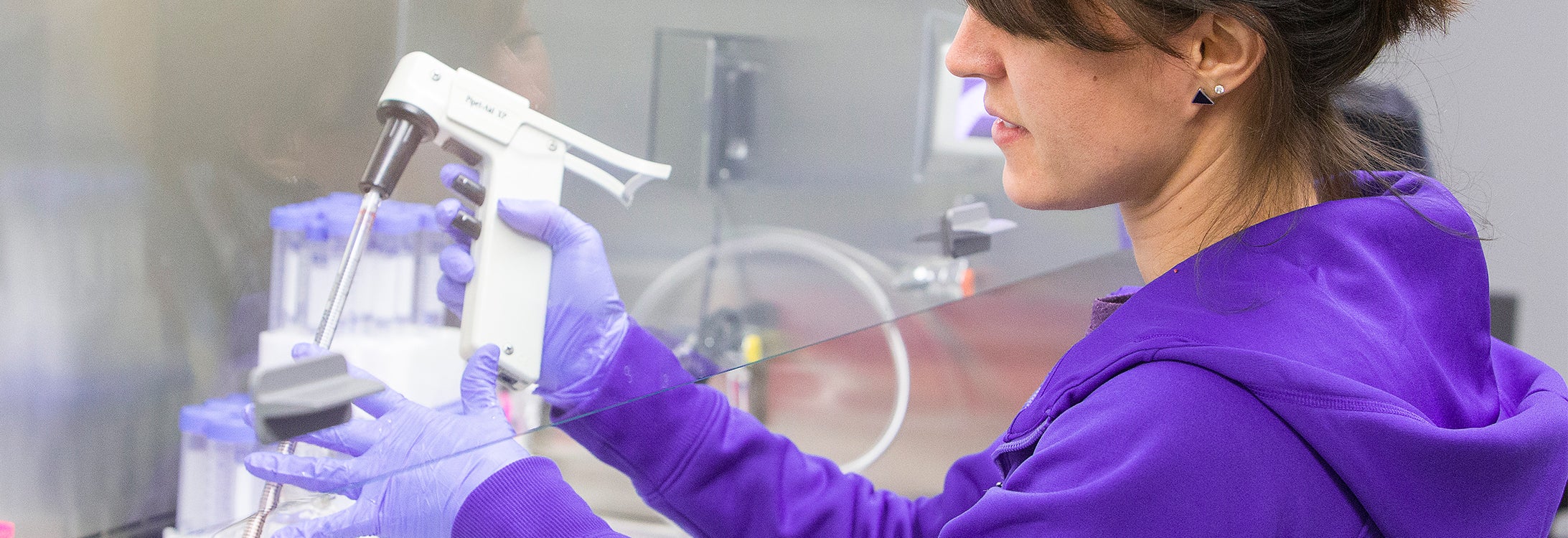 A picture of a person in a purple hoodie holding a piece of lab equipment.