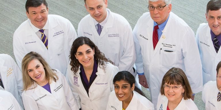 An image depicting a top-down view of eleven scientists in lab coats. Each person's coat has text that reads 