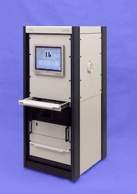 A picture taken in front of an indigo background of the EchoMRI-700 machine. It is rectangular in shape, and has a screen on one side. There are a few drawers and trays below the screen. The main body of the device is white, and it has black accents.