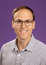An image of Dr. Nicholas Broskey. He has pale skin and brown hair, and wears glasses. He is smiling in the image, which was taken in front of a purple background.