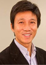 An image of Dr. Hu Huang. He has tanned skin and dark brown hair. He wears a suit, and is smiling brightly.