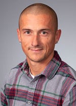 An image of Dr. Kelsey Fisher-Wellman. He has tanned skin, earrings, and a buzz cut. He is smiling.