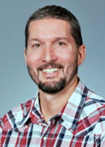 An image of Dr. Christopher Geyer, who is smiling brightly. He has brown hair and a beard.