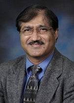An image of Dr. Laxmansa Katwa. He has black hair, a moustache, and mid-tone dark skin. He is wearing a gray suit and a gray patterned tie.