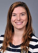 An image of Dr. Lisandra de Castro Brás. She has long red hair and pale skin. She wears a striped black-and-white shirt, as well as a necklace.