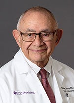 An image of Dr. Walter Pories. He has tanned skin, short gray hair, and is wearing glasses. In the image, he is shown wearing a lab coat with the ECU Physicians logo on it.