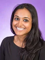 An image of Dr. Bhibha Das. She has long black hair, mid-tone brown skin, and is smiling brightly. She is wearing a black shirt, and the image was taken in front of a purple background.