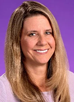 An image of Dr. Jennifer Hodgson. She has long blonde hair and pale skin, and is smiling. Her picture was taken in front of a purple background.