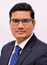 An image of Dr. Srinivas Sriramula. He has black hair, tanned skin, and glasses. He wears a black suit and a blue striped tie.