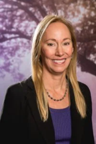 An image of Dr. Rachel Roper. She has long blonde hair, tanned skin, and is smiling. She is standing in front of background depicting a flowering sakura tree.