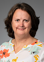 An image of Dr. Tracy Woodlief. She has tanned skin and mid-length brown hair. She is wearing a flowery shirt and smiling.