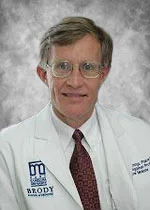 An image of Dr. Doyle Cummings. He has pale skin, gray-brown hair, glasses, and is smiling. He wears a lab coat with the 'Brody School of Medicine' logo on it, as well as a red tie.
